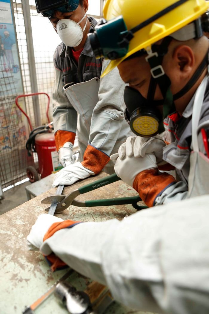 Two workers wearing safety gear while cutting metal in a workshop environment.